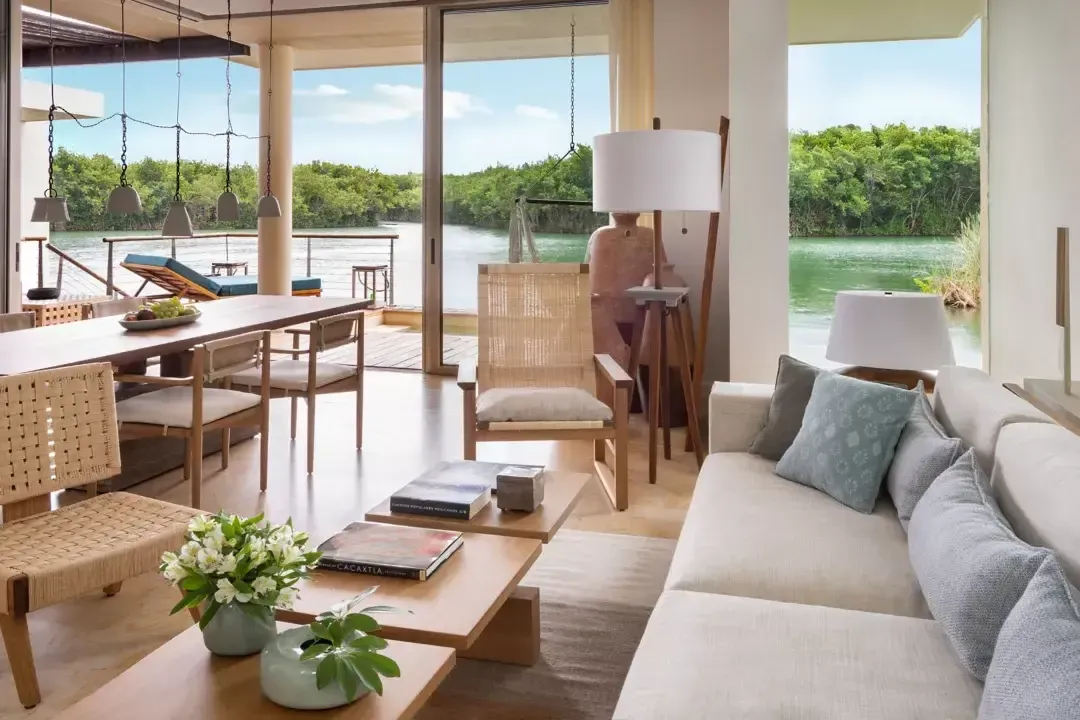 Rosewood Mayakoba, Mexico — Waterfront living room with woven furnishings, floor-to-ceiling windows, pendant lights, and mangrove lagoon views.