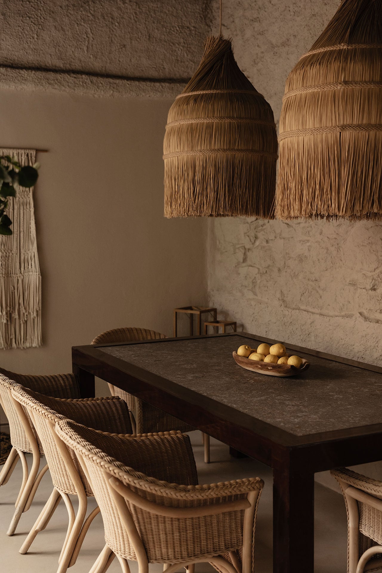 Casa Somos Sueños, Europe — Dining room with woven pendant lamps, rattan chairs, dark stone table, and textured plaster walls in warm neutral tones.