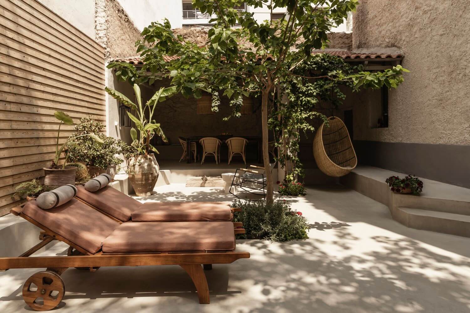 Casa Somos Suenos, Europe — Sunlit courtyard with wooden loungers, woven hanging chair, vine-covered pergola, and stone walls creating intimate Mediterranean-style outdoor living space.