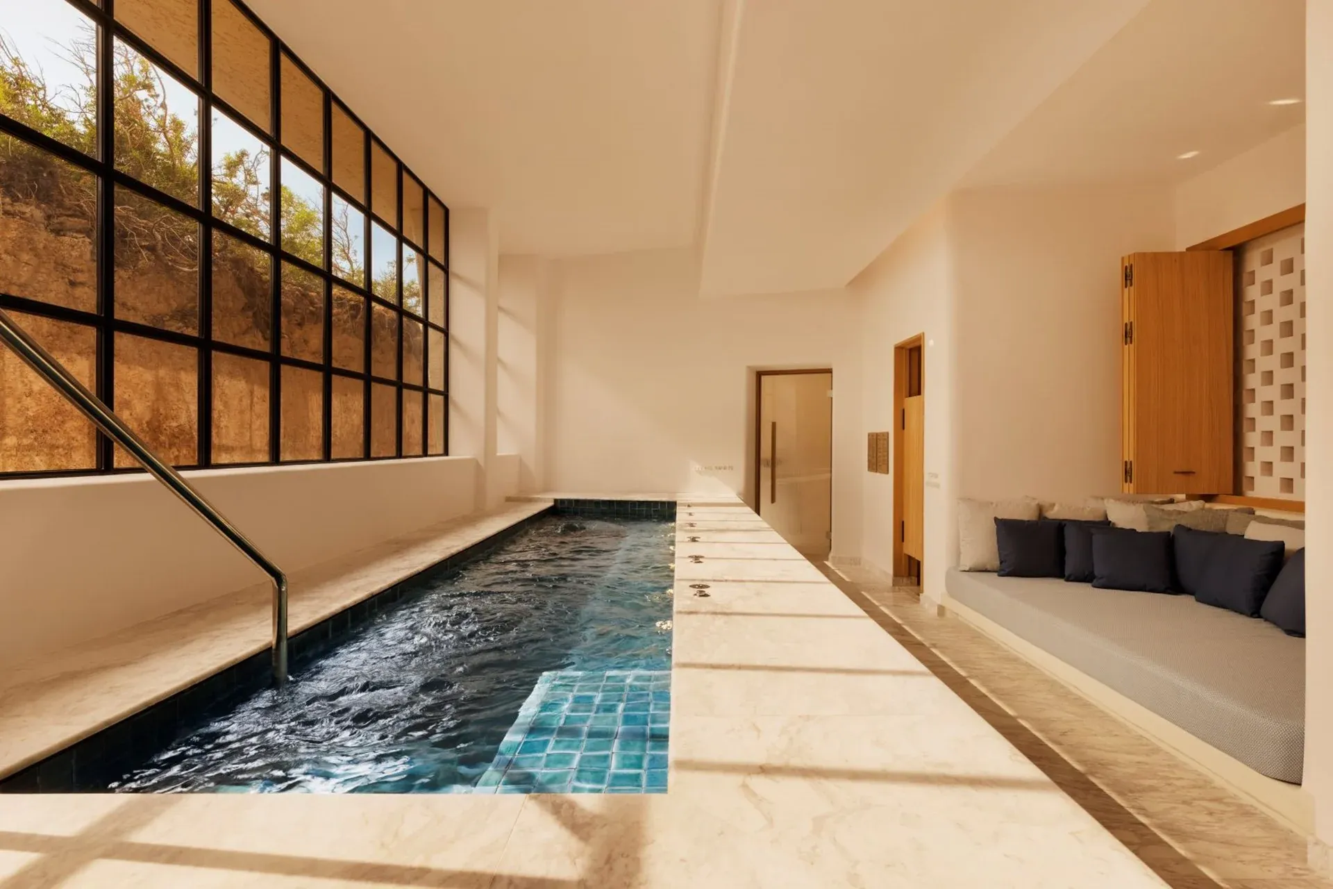 Six Senses Spa, Balearic Islands, Spain — Indoor swimming pool with turquoise tile accents, minimalist architecture, natural light through gridded windows, wooden details, spa lounging area.