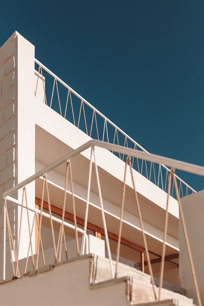 Casa Santa Teresa, Europe — Minimalist white balconies with geometric metal railings overlooking deep blue sea, strong sunlight casting sharp shadows on modern architecture.