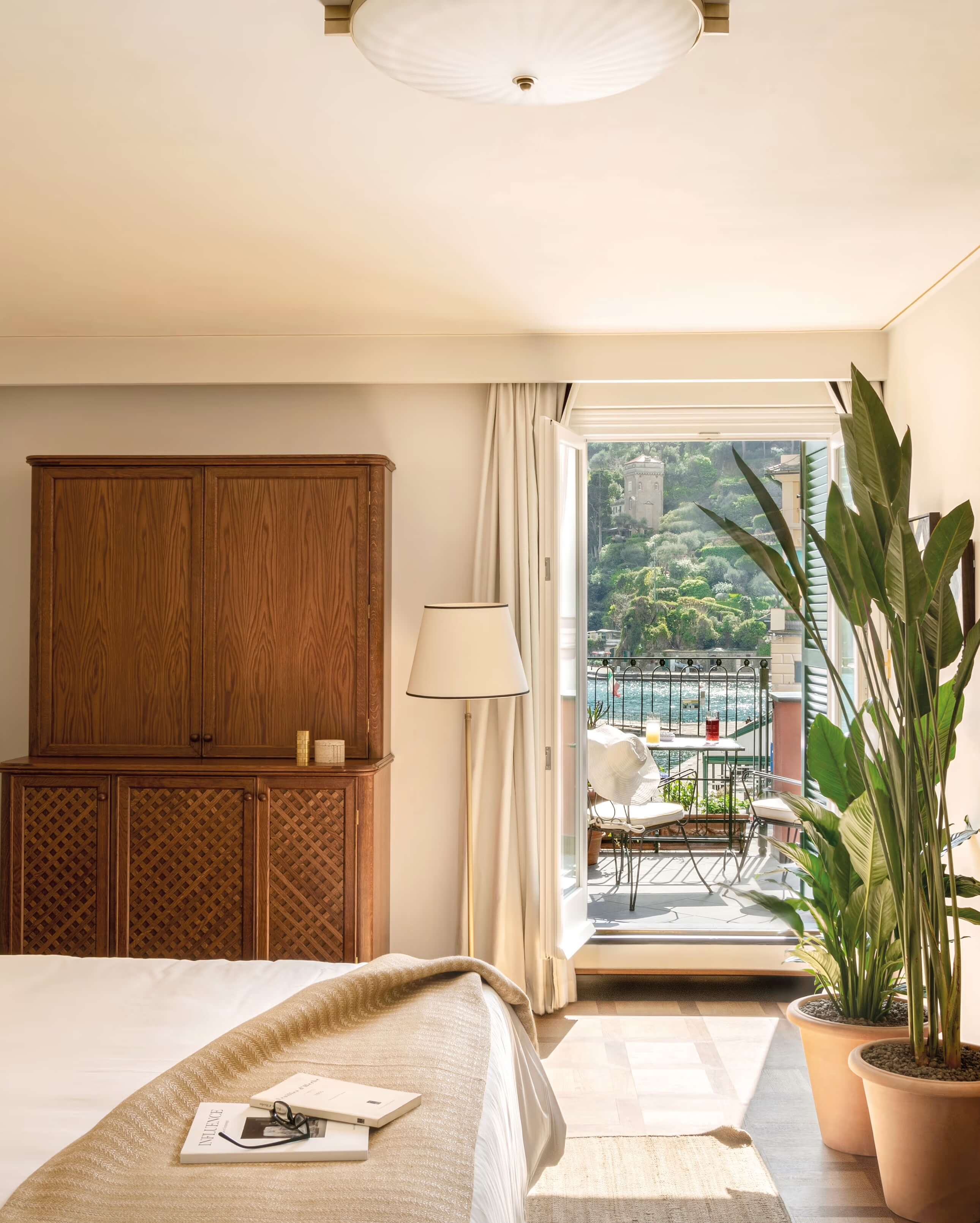 Splendido Mare, Europe — Luxury bedroom with wooden cabinetry, terracotta plants, cream linens, and Mediterranean balcony overlooking hillside gardens and sea.