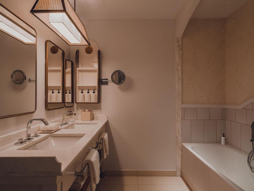 Carlton Cannes, Europe — Minimalist bathroom with dual marble vanity, bronze-framed mirrors, terrazzo flooring, and soaking tub in warm neutral palette.