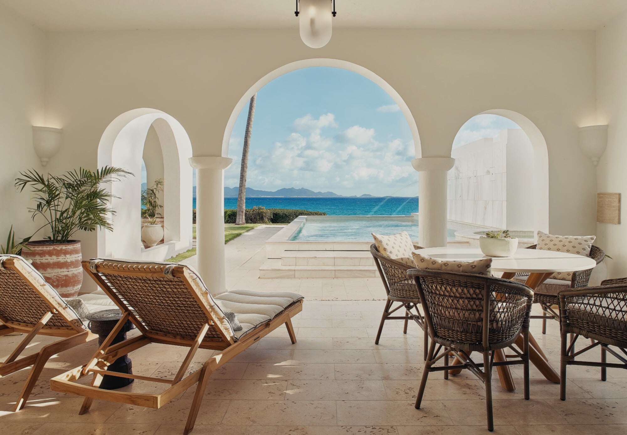 Cap Juluca, Anguilla — Whitewashed arched portico with rattan loungers overlooking infinity pool and Caribbean Sea, minimalist coastal luxury architecture.