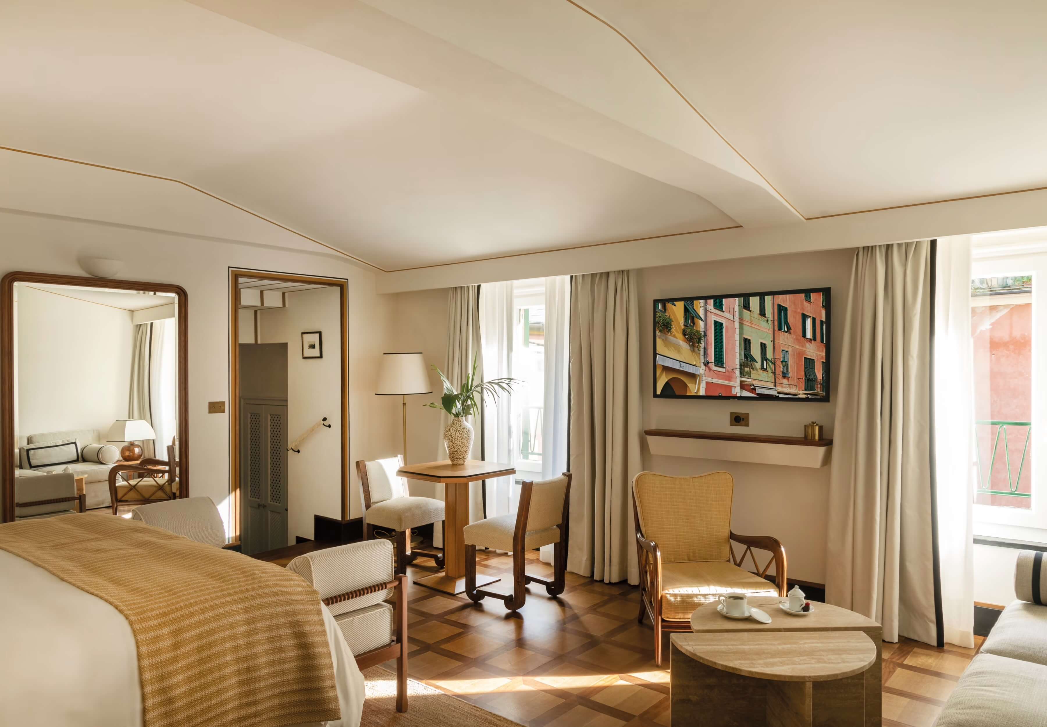 Splendido Mare, Europe — Luxury hotel suite with wooden furnishings, cream upholstery, floor-to-ceiling windows, warm natural light, and contemporary coastal design aesthetic.
