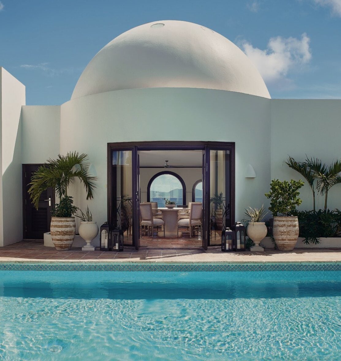 Cap Juluca, North America — White dome architecture with dark-framed glass doors overlooking turquoise pool, palm planters, and sea view.