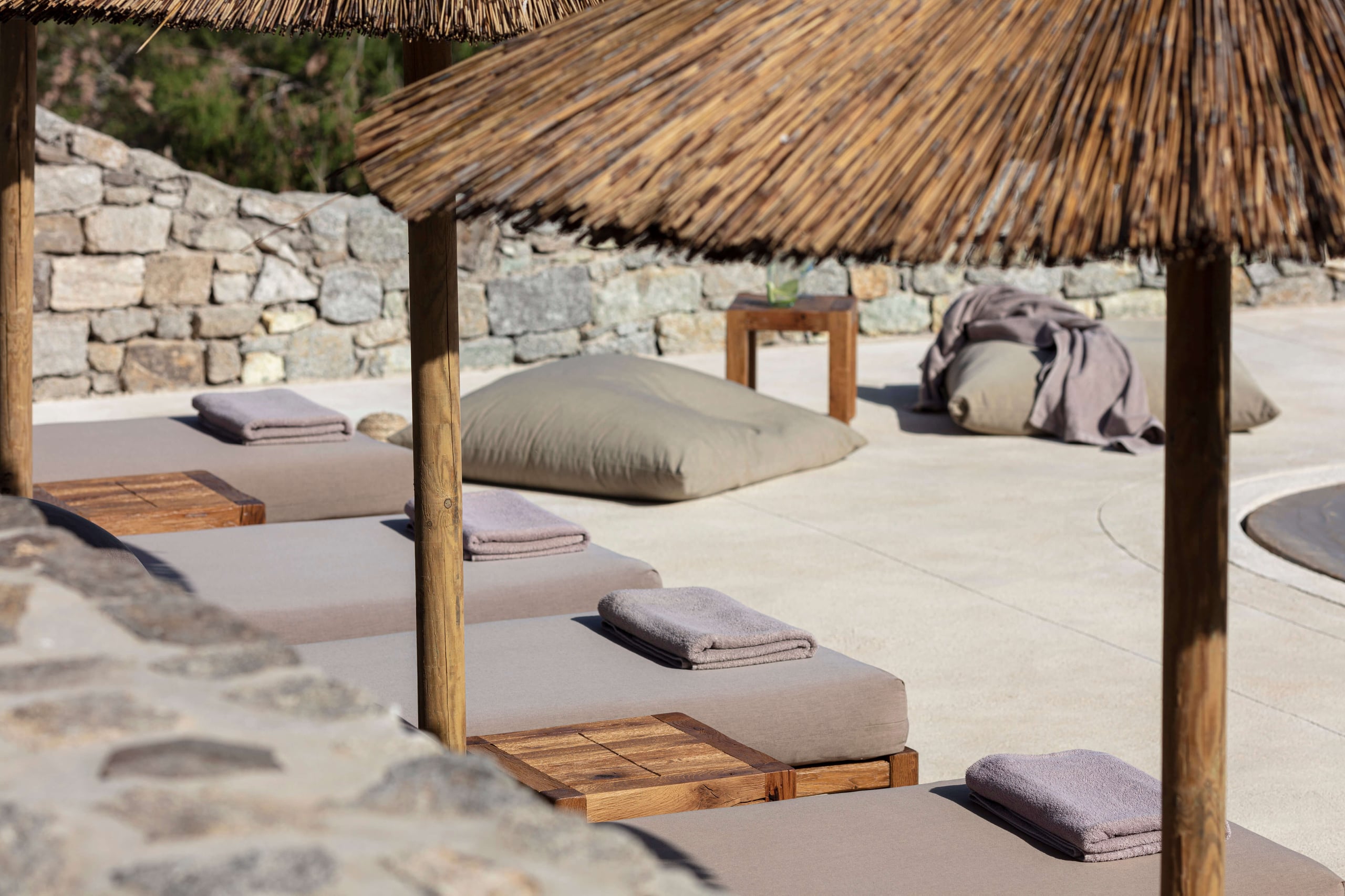 Villa Tama, Europe — Thatched-roof yoga pavilion with cushioned mats, wooden platforms, and stone walls overlooking terrace in minimalist wellness retreat setting.