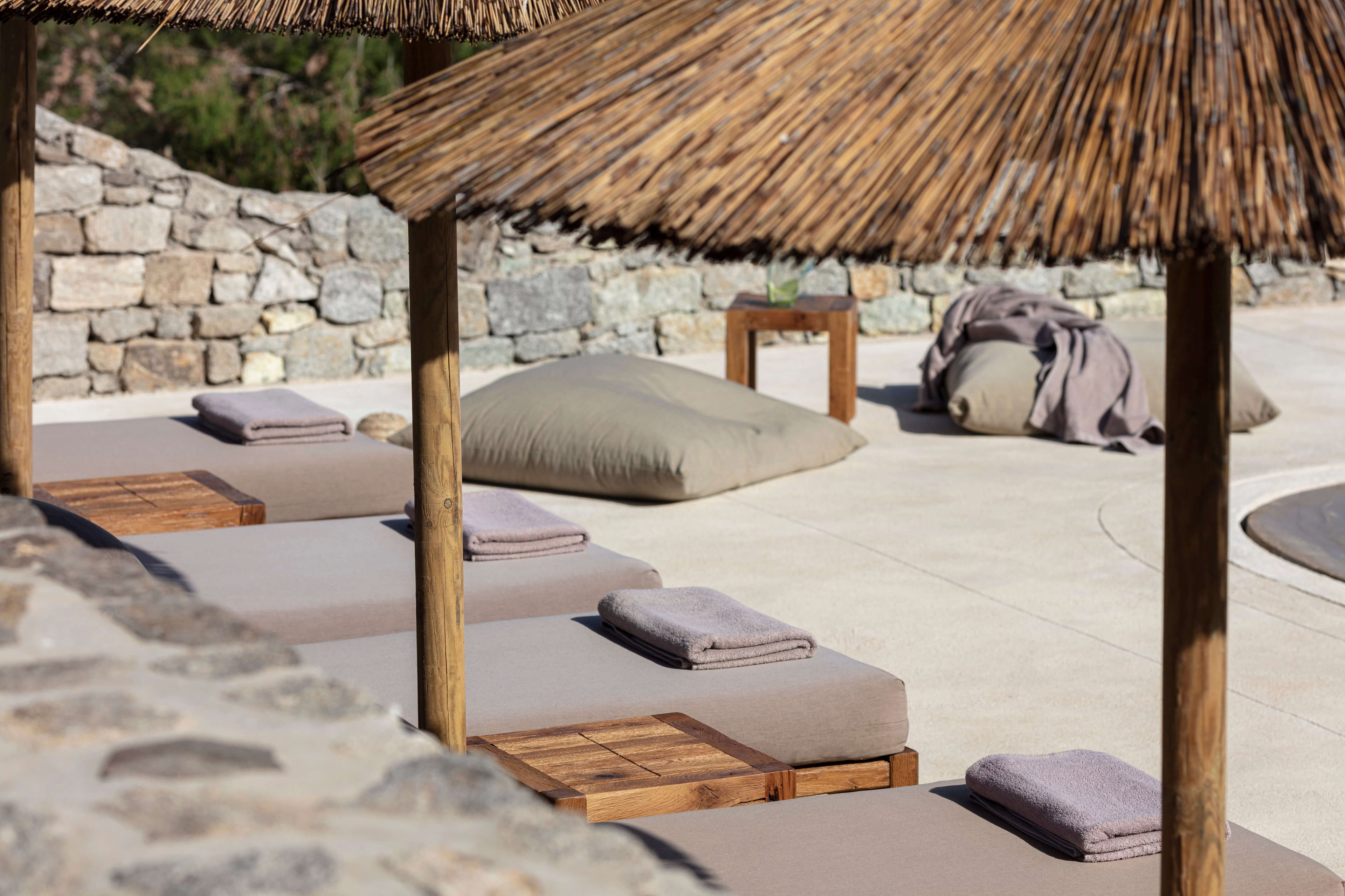 Villa Tama, Europe — Thatched-roof yoga pavilion with cushioned mats, wooden platforms, and stone walls overlooking terrace in minimalist wellness retreat setting.
