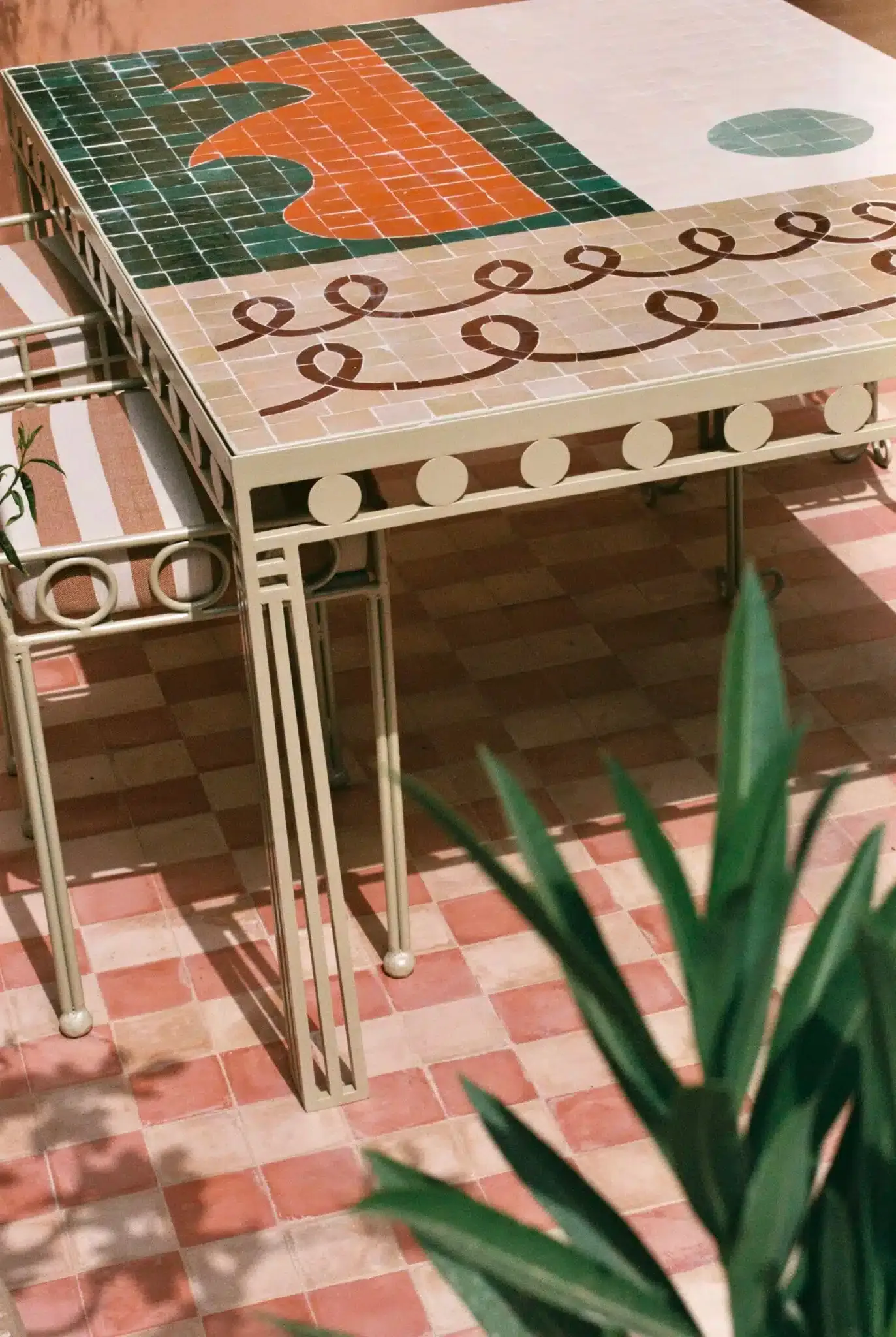 Rosemary, Africa — Geometric tile table with orange pattern, cream and green detailing, metal frame, sunlit terracotta floor, minimalist hospitality design.