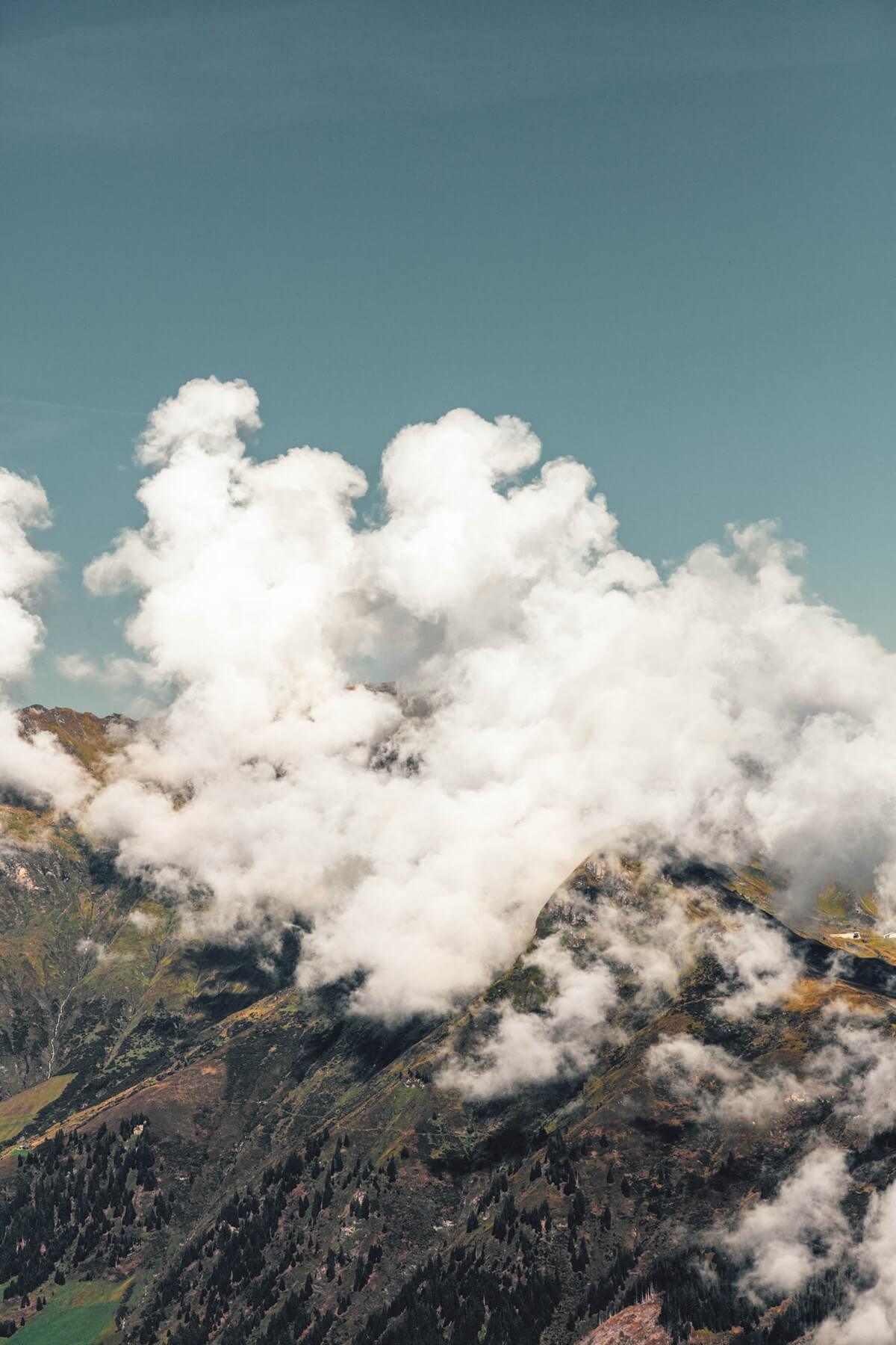 The Cōmodo — Cōmodo, Europe — Cumulus clouds rise above forested alpine mountains under clear blue sky, dramatic landscape photography.