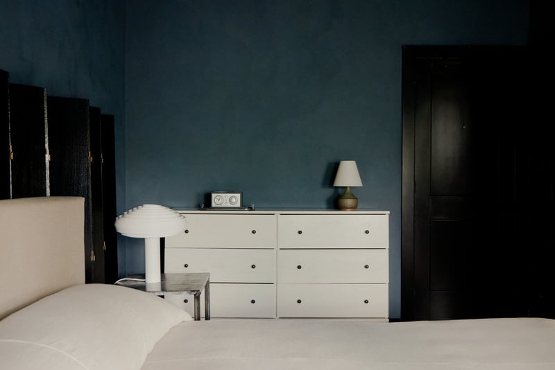The James Bradley, North America — Minimalist bedroom with teal walls, cream dresser, black accents, and layered lighting creating serene luxury hospitality ambiance.