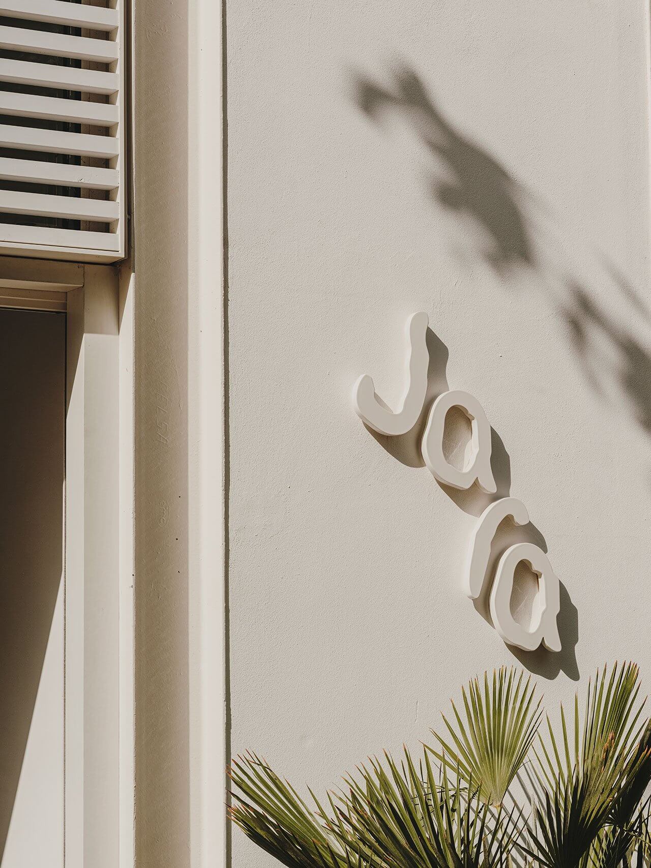 The Standard Ibiza, Balearic Islands, Spain — White sculptural wall signage with shadow detail above palm fronds, minimalist hospitality architecture in bright sunlight.
