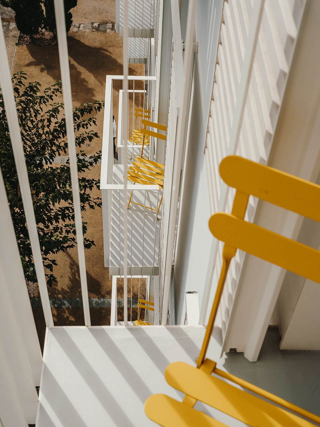 The Standard Ibiza, Balearic Islands, Spain — Yellow chairs on striped terrace overlooking minimalist courtyard with white walls and verdant climbing vines.