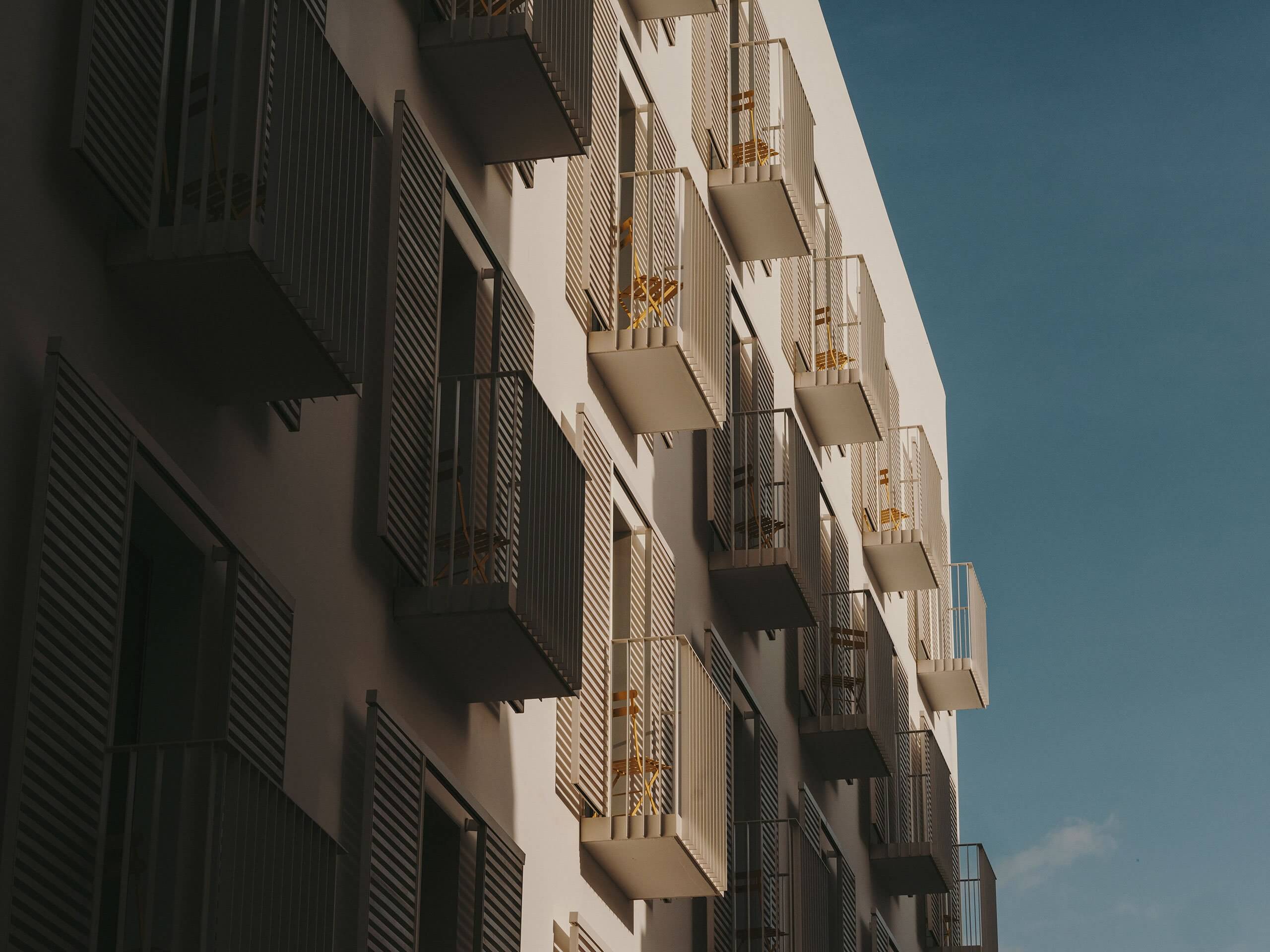 The Standard Ibiza, Balearic Islands, Spain — Modernist residential facade with stacked balconies, ribbed metal screens, and geometric shadows under clear sky.