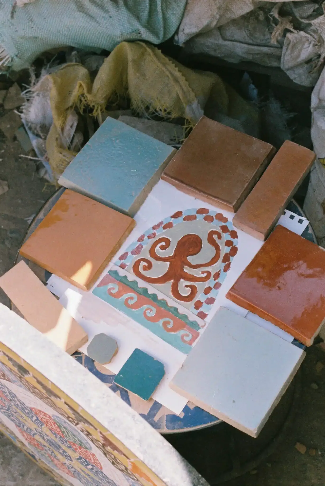 Rosemary, Africa — Terracotta tile samples and hand-painted ceramic designs arranged on white surface, showcasing warm earth tones and decorative patterns.