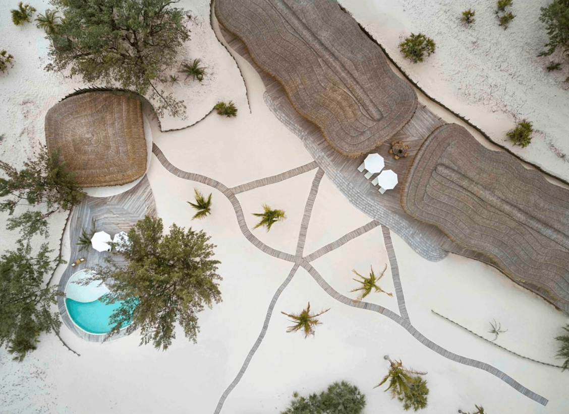 Kisawa Sanctuary, Africa — Aerial view of luxury resort with wooden boardwalks, white sand, turquoise pool, scattered palms, and minimalist architecture in tropical setting.