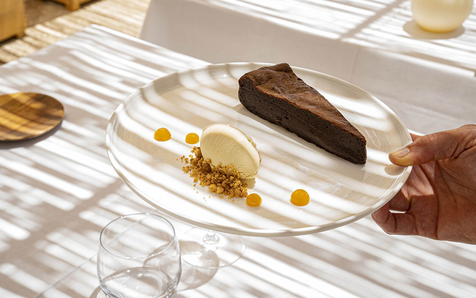 Torralbenc, Balearic Islands — Chocolate torte with vanilla ice cream, crispy crumble, and passion fruit spheres on white plate, dappled sunlight.