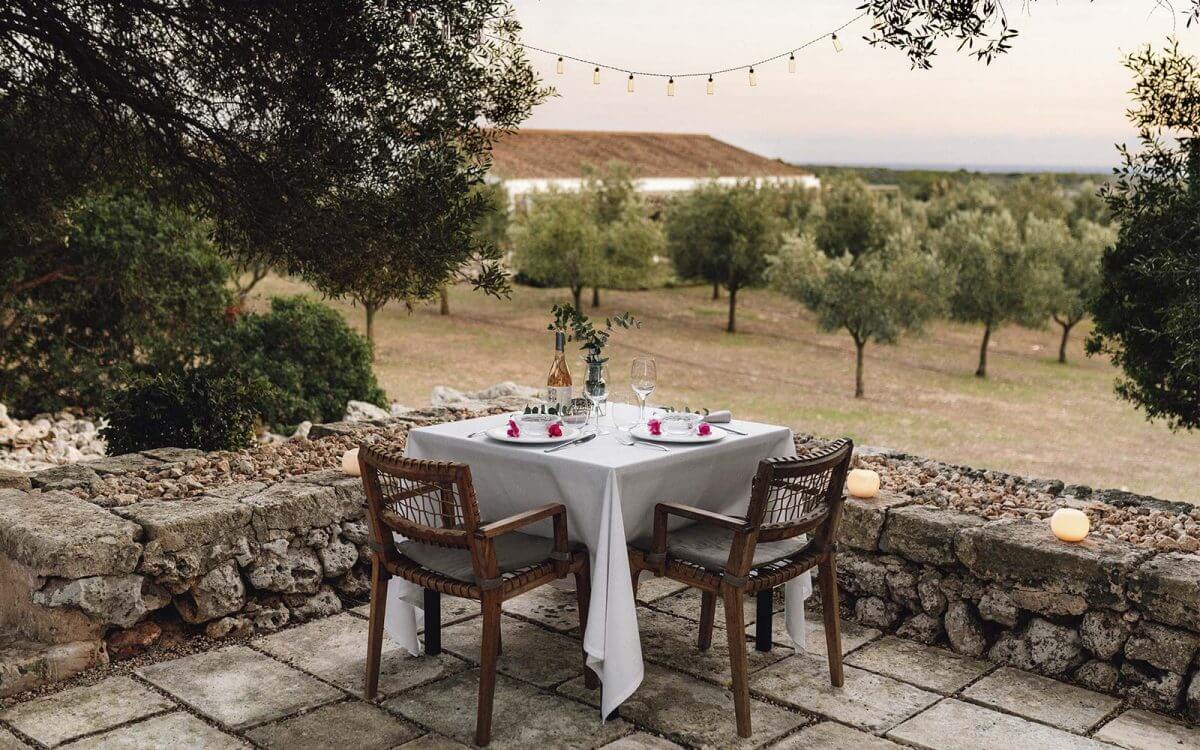 Torralbenc, Balearic Islands — Intimate stone terrace dinner setup overlooking olive groves at dusk, with string lights and candlelit ambiance.