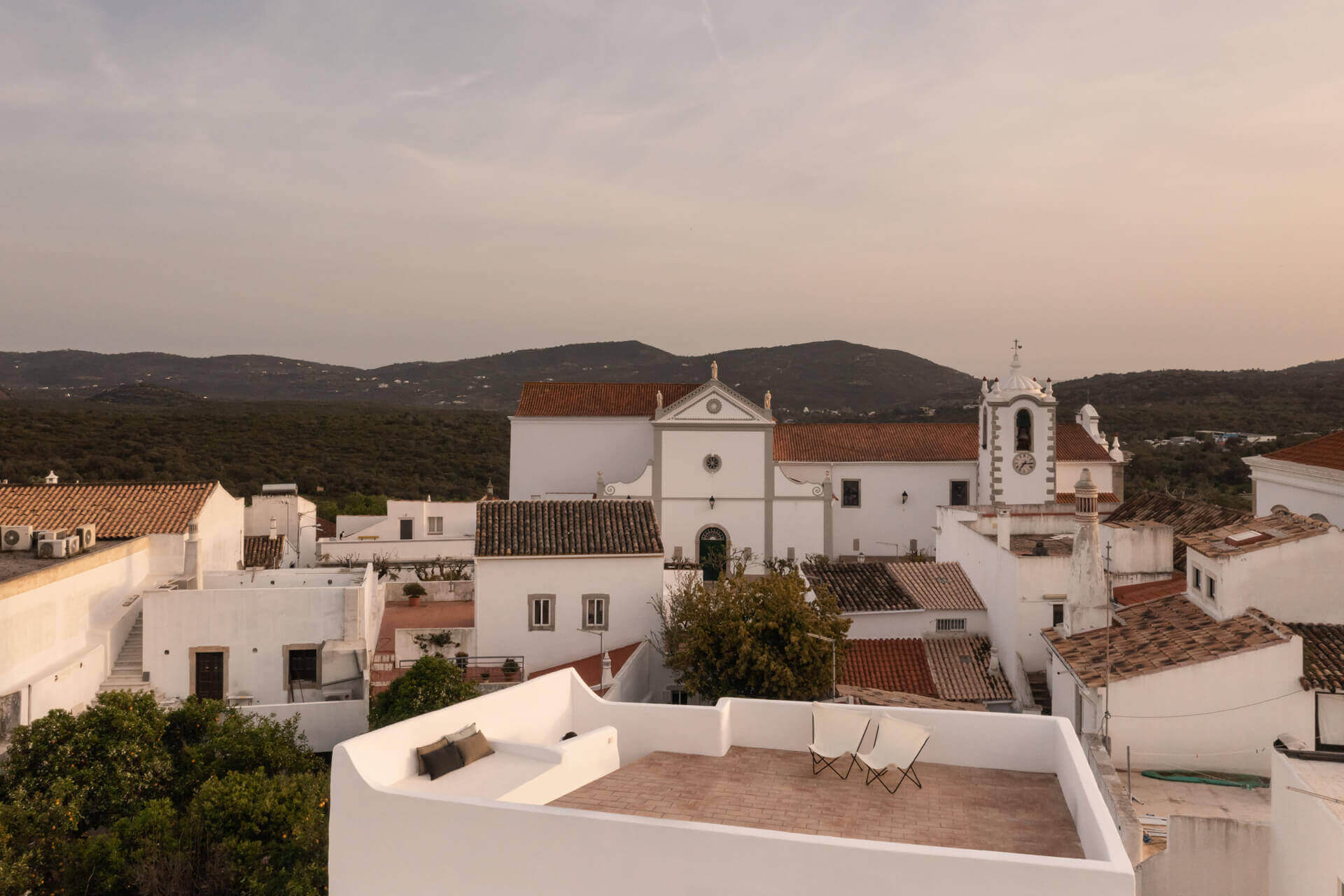 Casa Quatro, Europe — Whitewashed rooftop terrace with terracotta tiles overlooking Andalusian village architecture and rolling hills at sunset.
