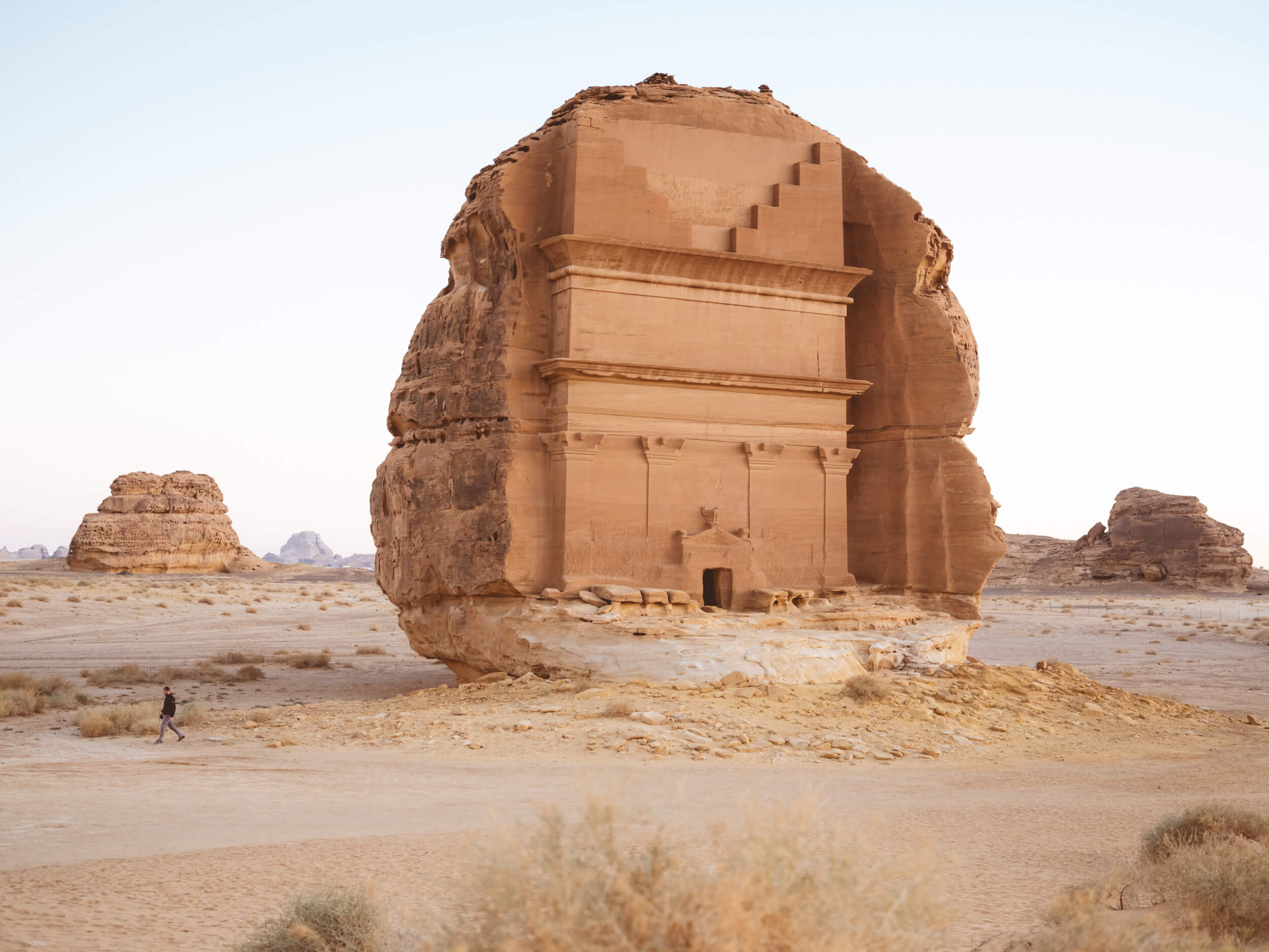 Habitas AlUla, Saudi Arabia — Ancient sandstone tomb carved into desert rock beneath clear sky, architectural heritage amid arid landscape.