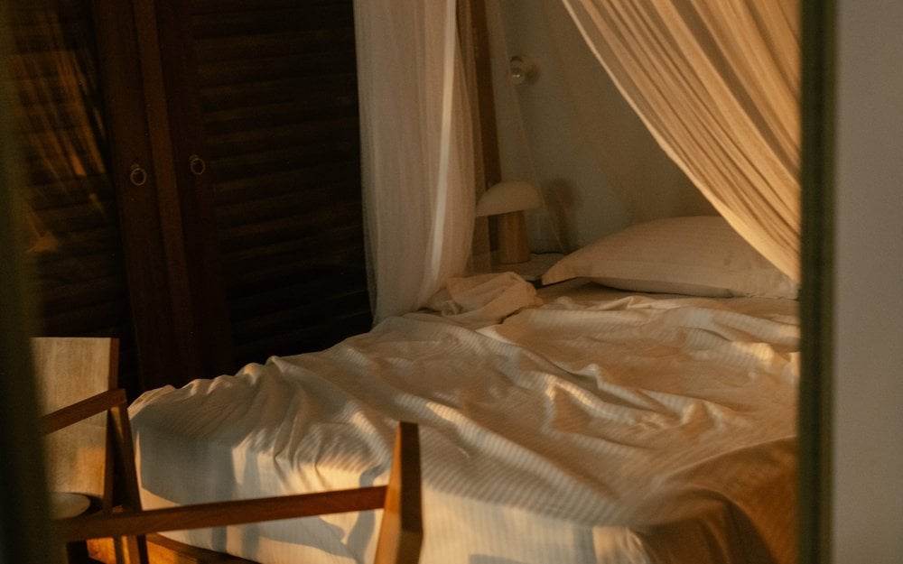 Kurulu Bay, Asia — Sunlit bedroom with sheer curtains, neutral linens, and wooden furniture casting soft shadows through golden afternoon light.
