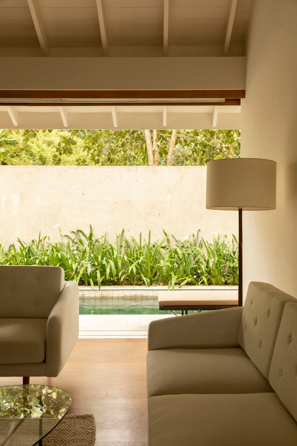 Kurulu Bay, Asia — Modernist pavilion with exposed beam ceiling, neutral linen seating, and framed view of manicured garden and infinity pool.