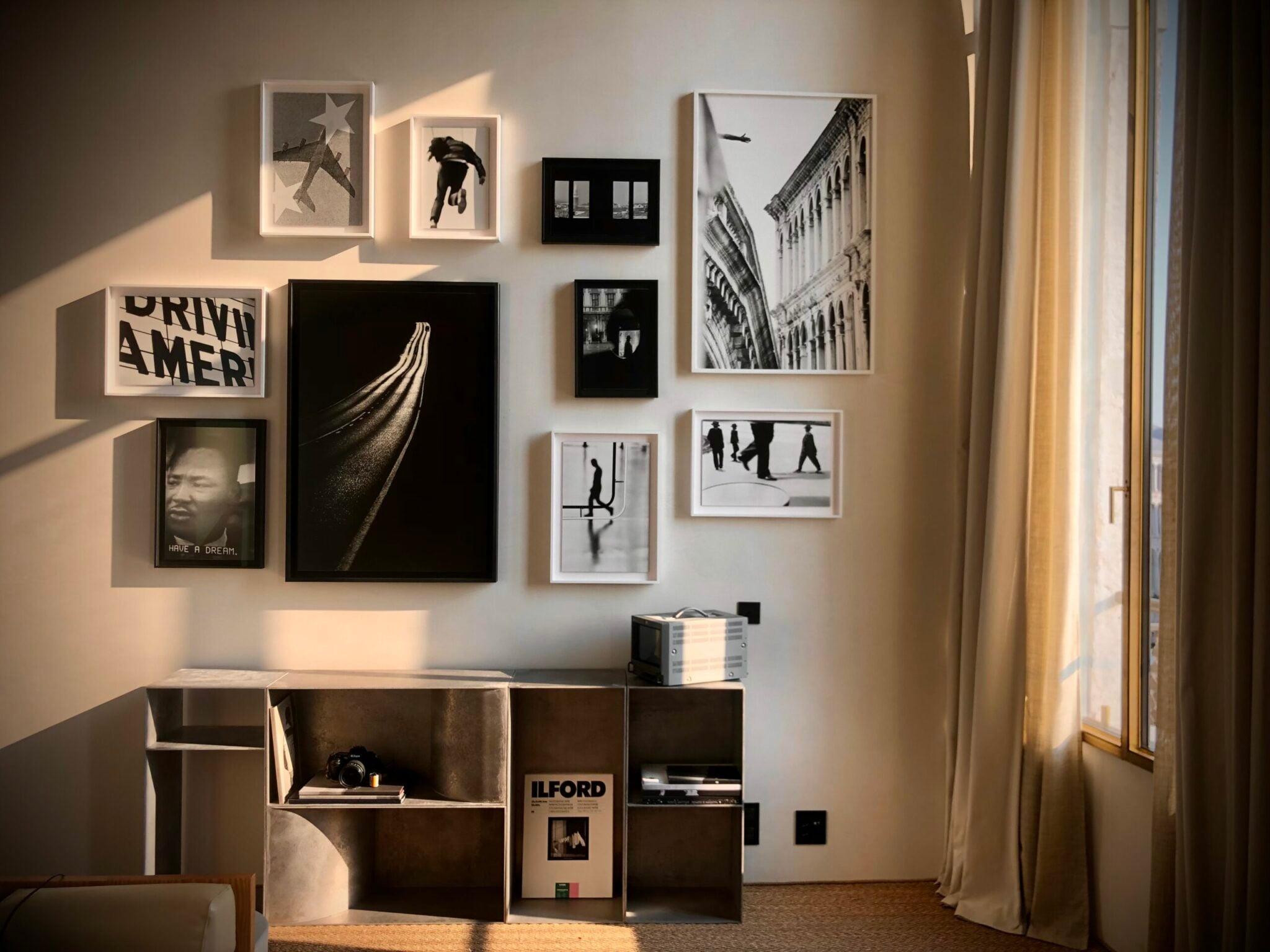 The Venice Venice Hotel, Venice, Europe — Black and white gallery wall with architectural photography, silhouettes, and typography above minimalist shelving unit in natural light.