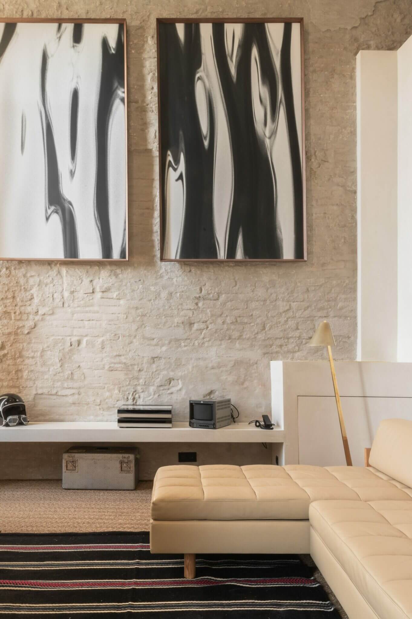 The Venice Venice Hotel, Europe — Minimalist bedroom with textured brick wall, abstract black and white framed art, cream upholstered seating, and floating shelf with curated objects.