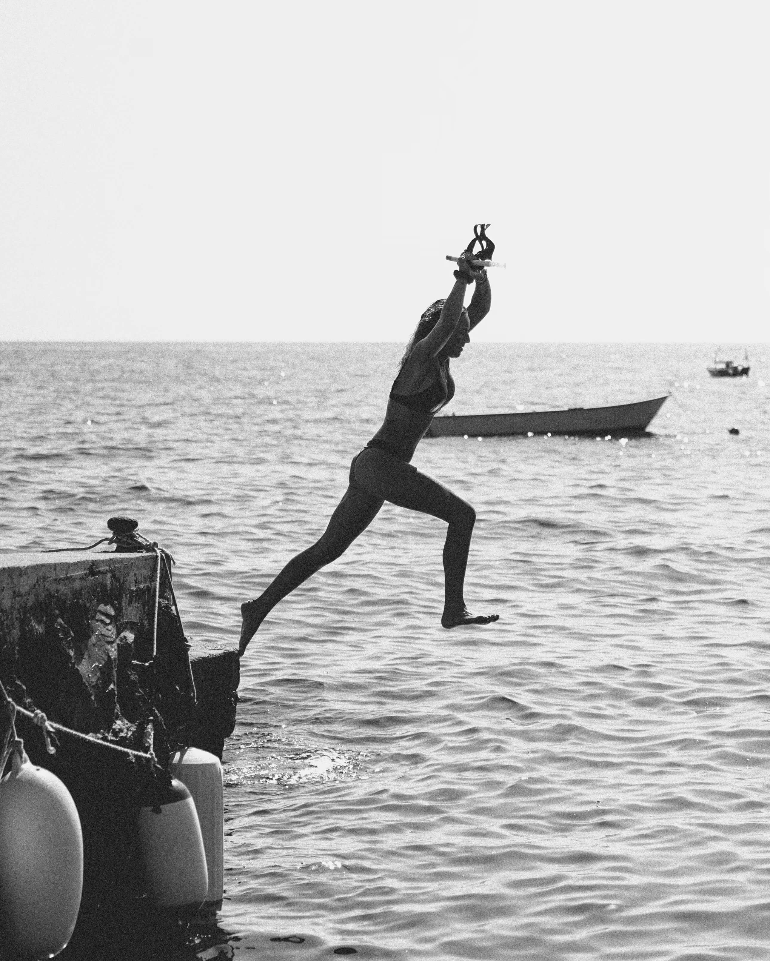 Splendido Mare, Europe — Diver in wetsuit leaping from wooden boat into calm Mediterranean waters, black and white coastal photography.