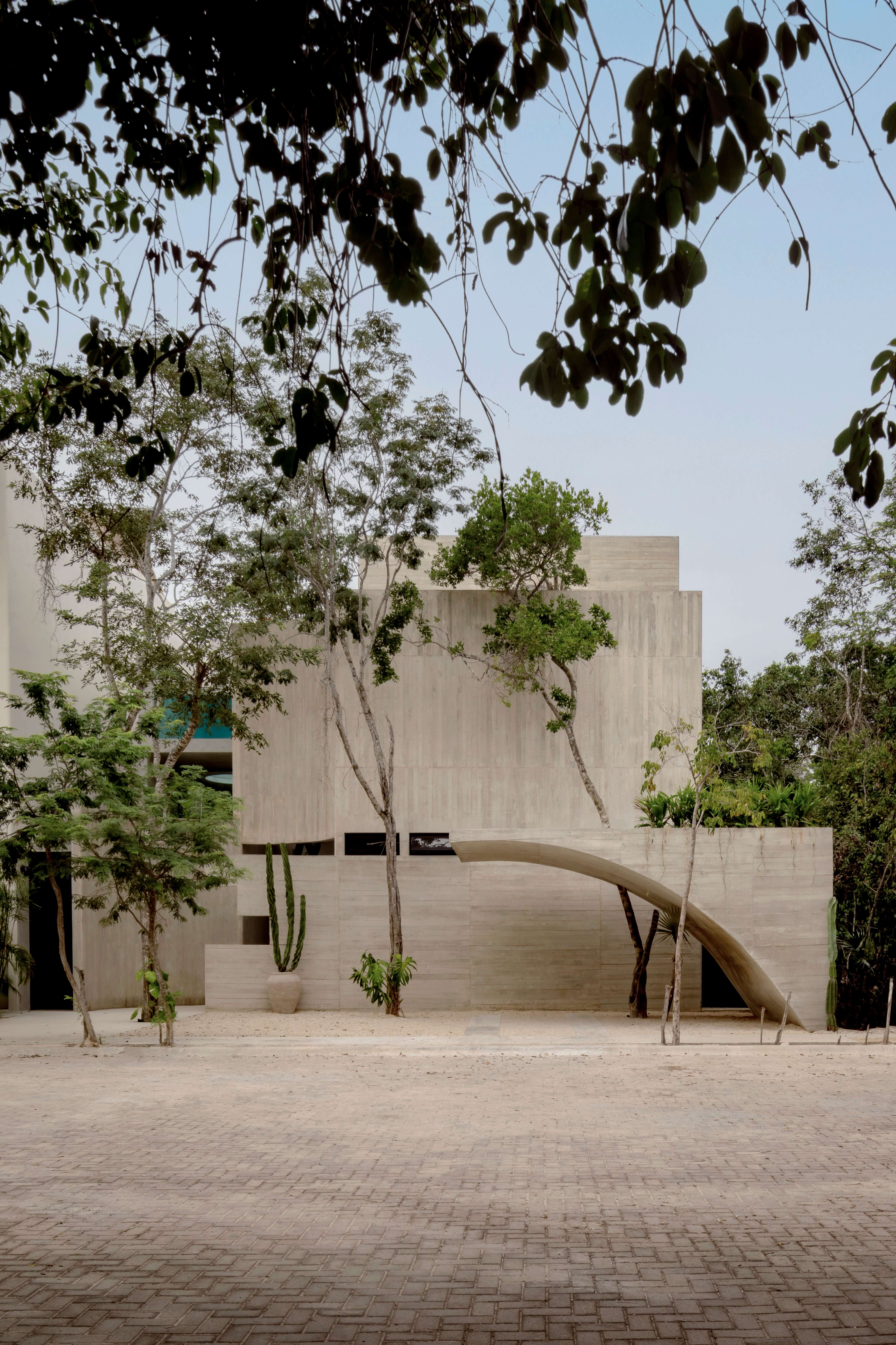 Villa Cava, Mexico — Minimalist concrete residence with curved archway, native trees, and geometric facade in desert courtyard setting.