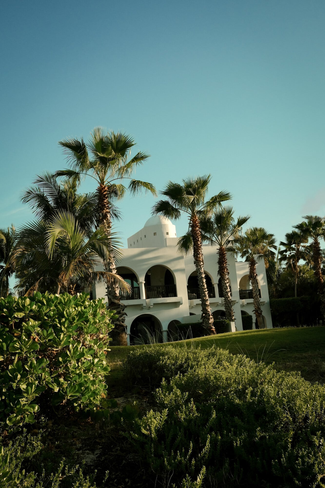 Cap Juluca, North America — Whitewashed Moorish architecture with domed roofline framed by palm trees and Mediterranean plantings under clear sky.