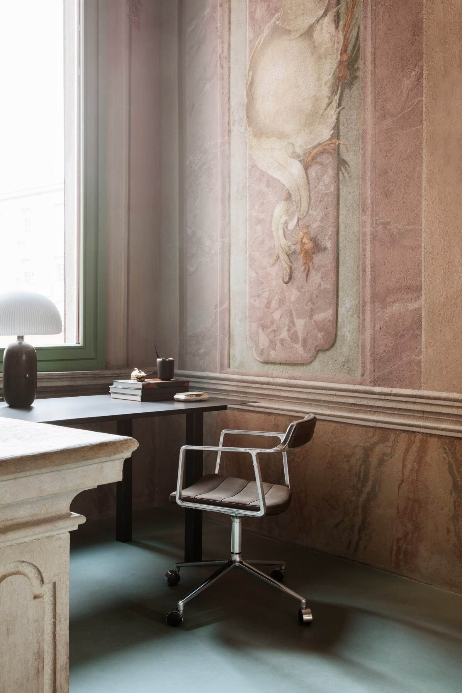 Vipp Palazzo Monti, Italy — Minimalist desk workspace with travertine architectural details, terracotta frescoed walls, and modernist chair beside arched window.