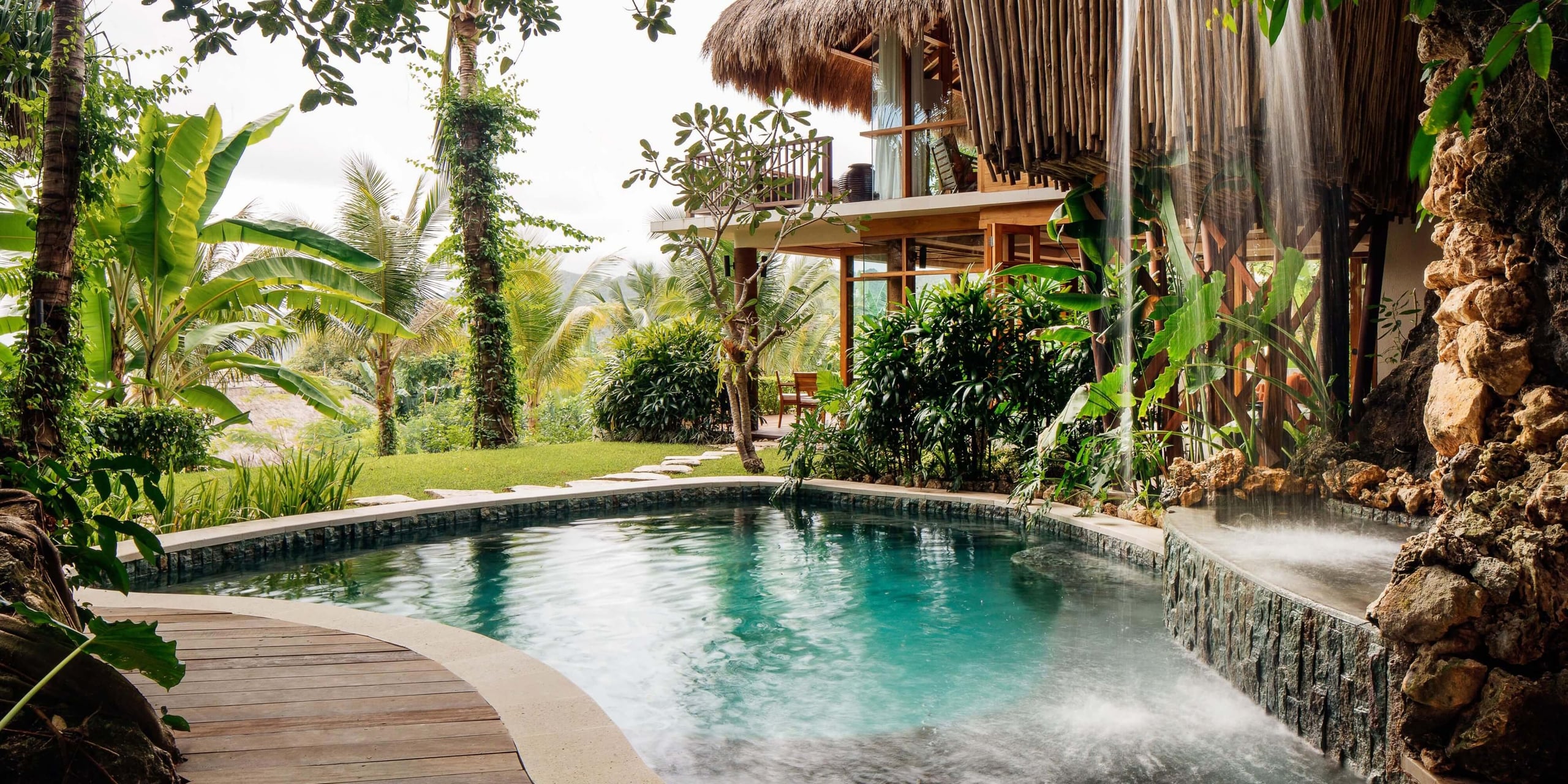 NIHI Sumba, Bali, Indonesia — Tropical villa with teak deck, turquoise pool, cascading waterfall, lush gardens, and open-air pavilion architecture.