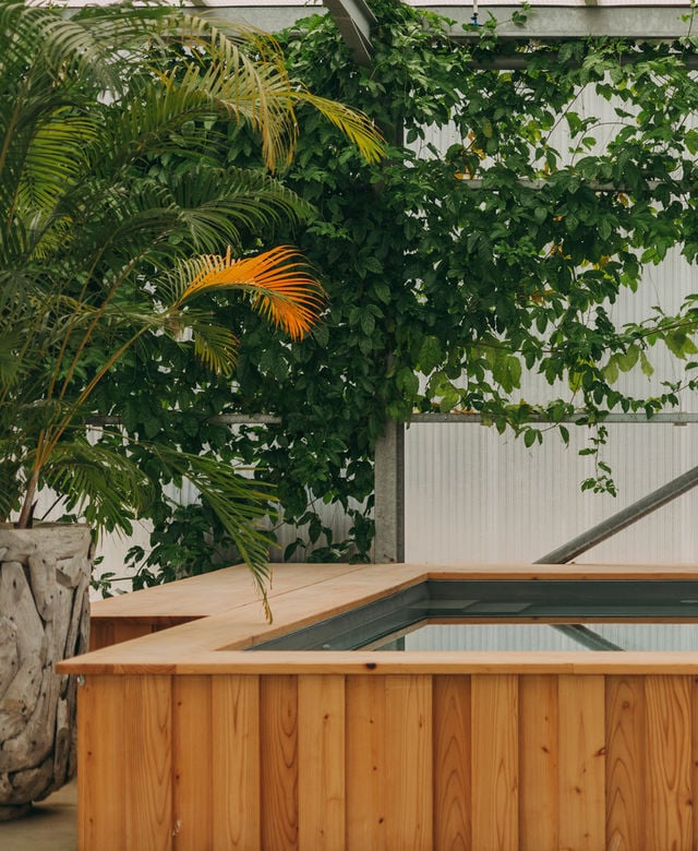 Wooden hot tub with tropical plants and corrugated metal backdrop at The Hut, Europe — luxury hospitality wellness design detail.