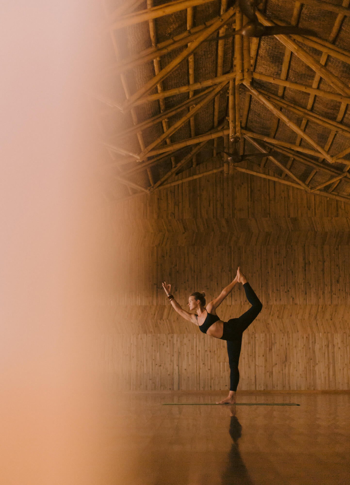 Cuixmala Spa, Mexico — Woman in natarajasana pose on yoga mat inside wooden barn with exposed timber beams and corrugated metal walls, warm golden light.